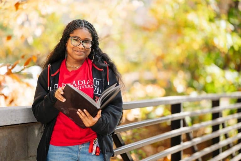 A student in a red Arcadia University shirt with an open book smiling at the camera