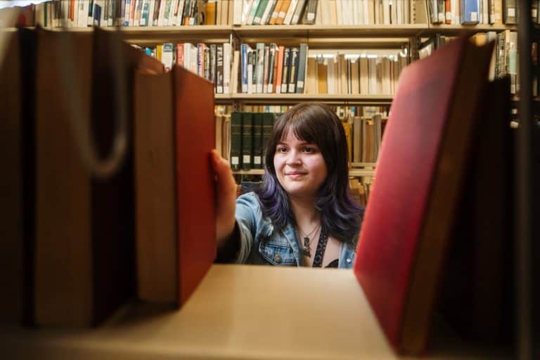 A student grabbing a book off of a library shelf