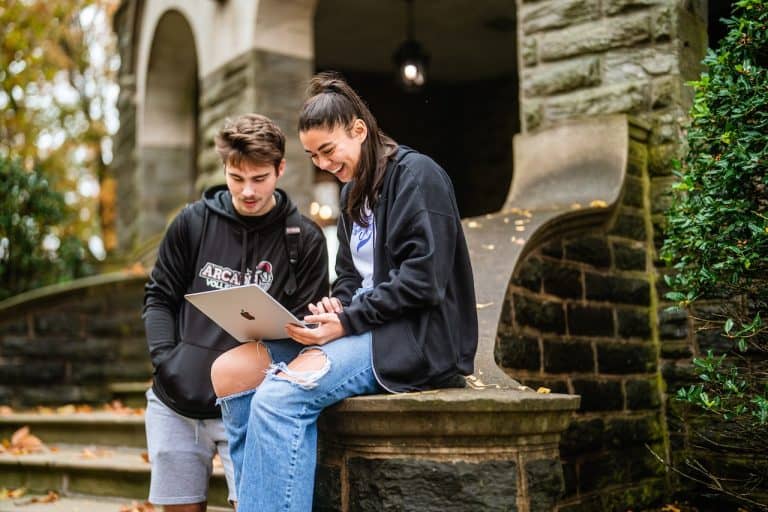 Two students sitting outside with one of them on her laptop